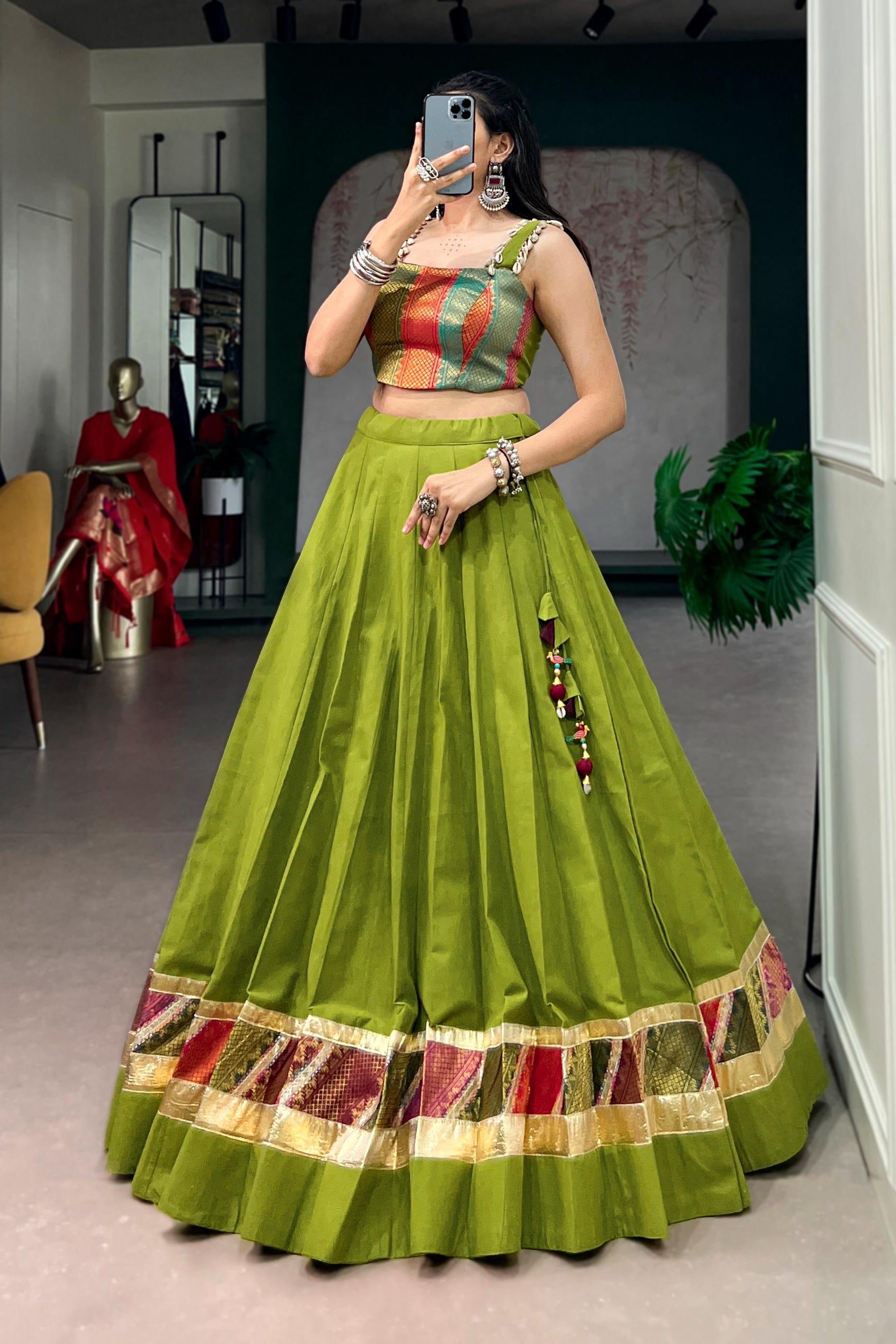 Woman taking a mirror selfie wearing a green traditional outfit with colorful patterns.