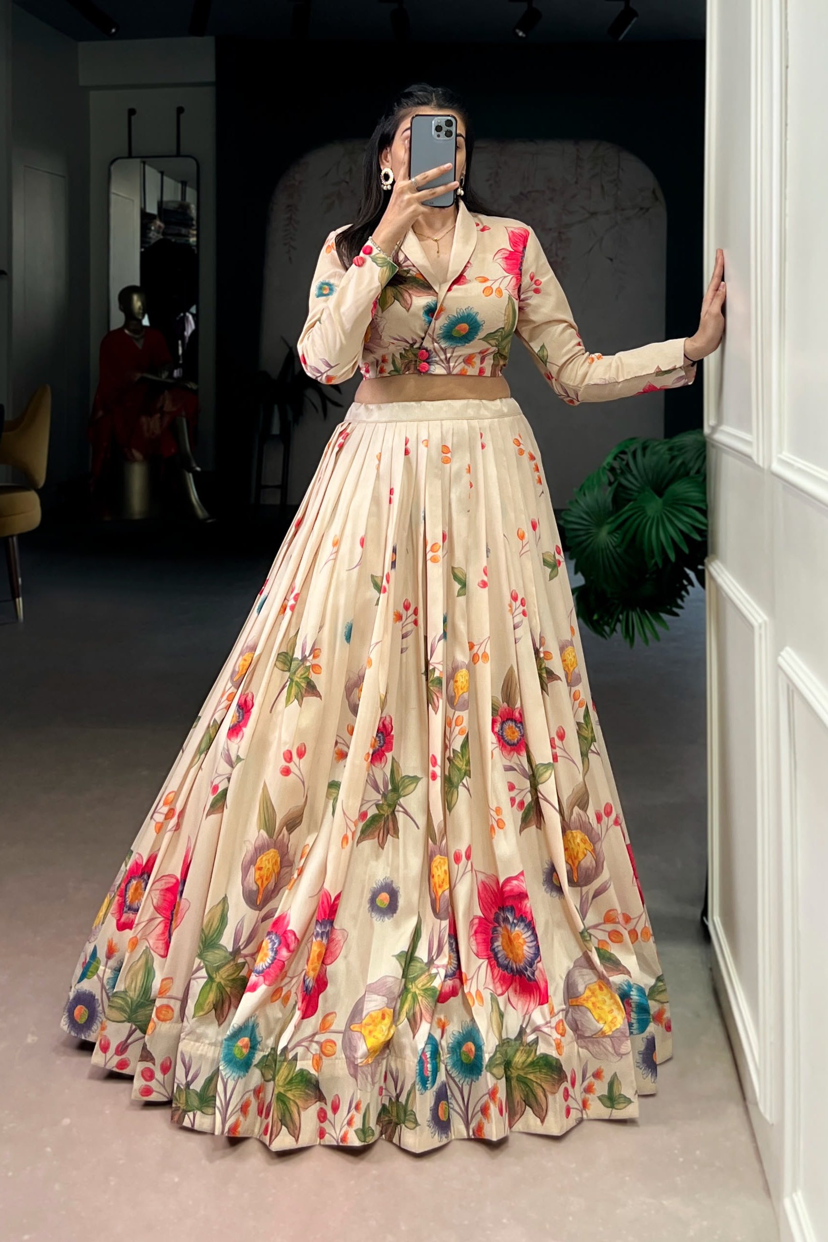 Woman wearing a floral dress taking a mirror selfie in a room.