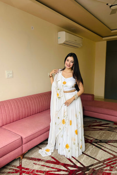 Woman in a white floral dress standing in a room with pink sofas and beige walls.
