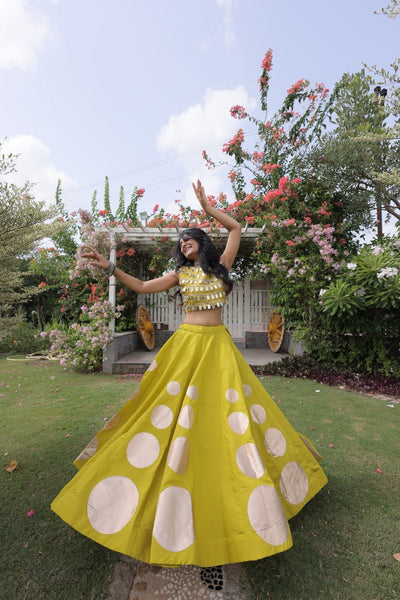 Woman in a yellow dress with white patterns standing in a garden.