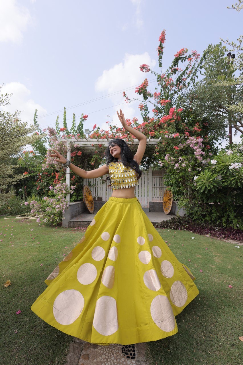 Woman in a yellow dress with white patterns standing in a garden.