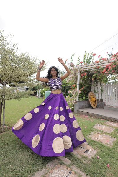 Woman in a purple skirt with gold circles dancing outdoors.