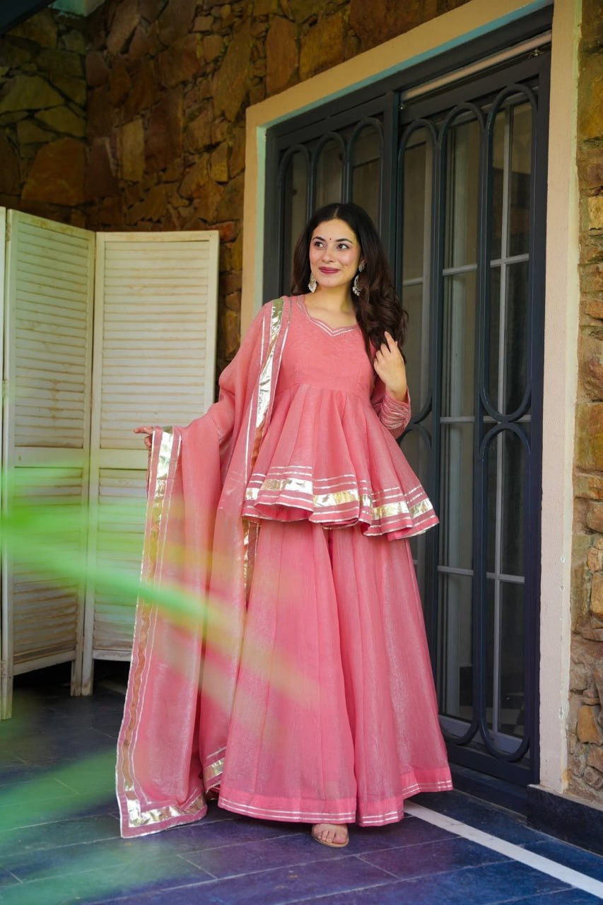 Woman in a pink traditional outfit standing in front of a stone wall.