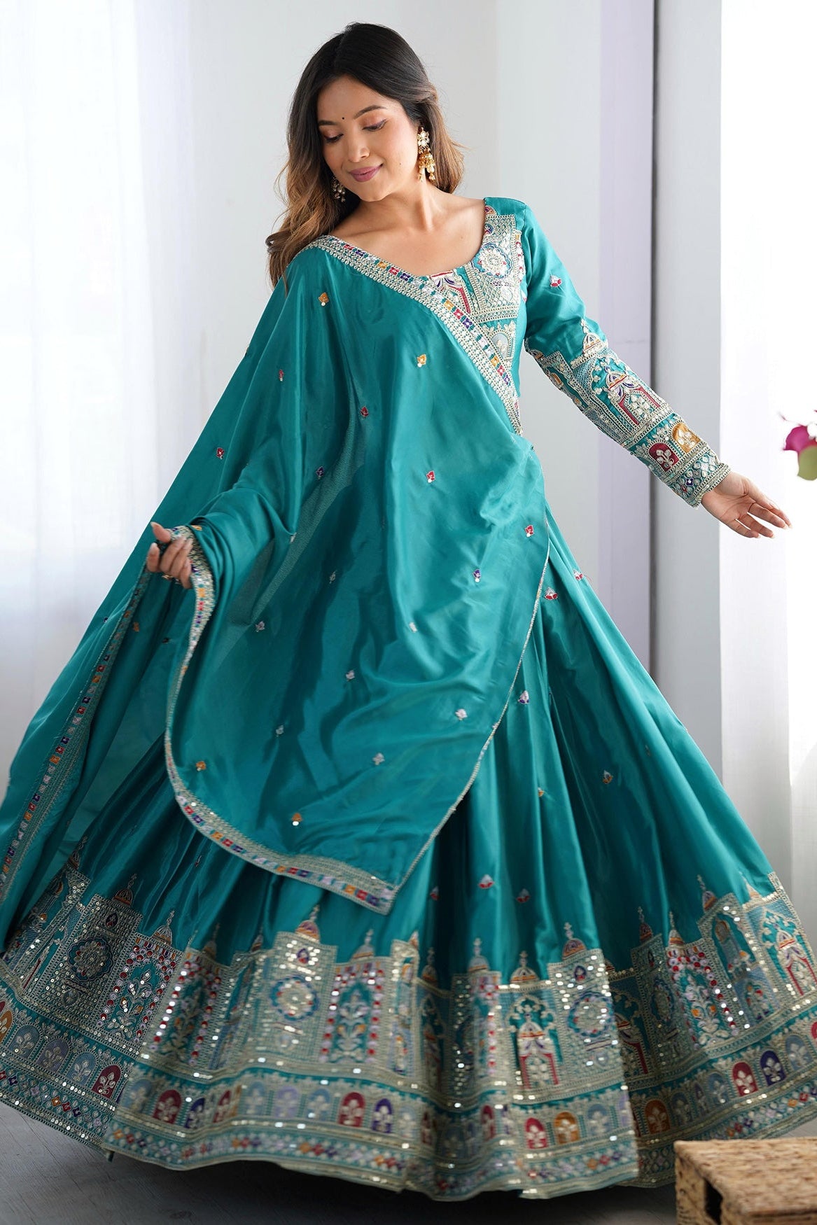 Woman wearing a teal traditional outfit with floral decorations indoors.