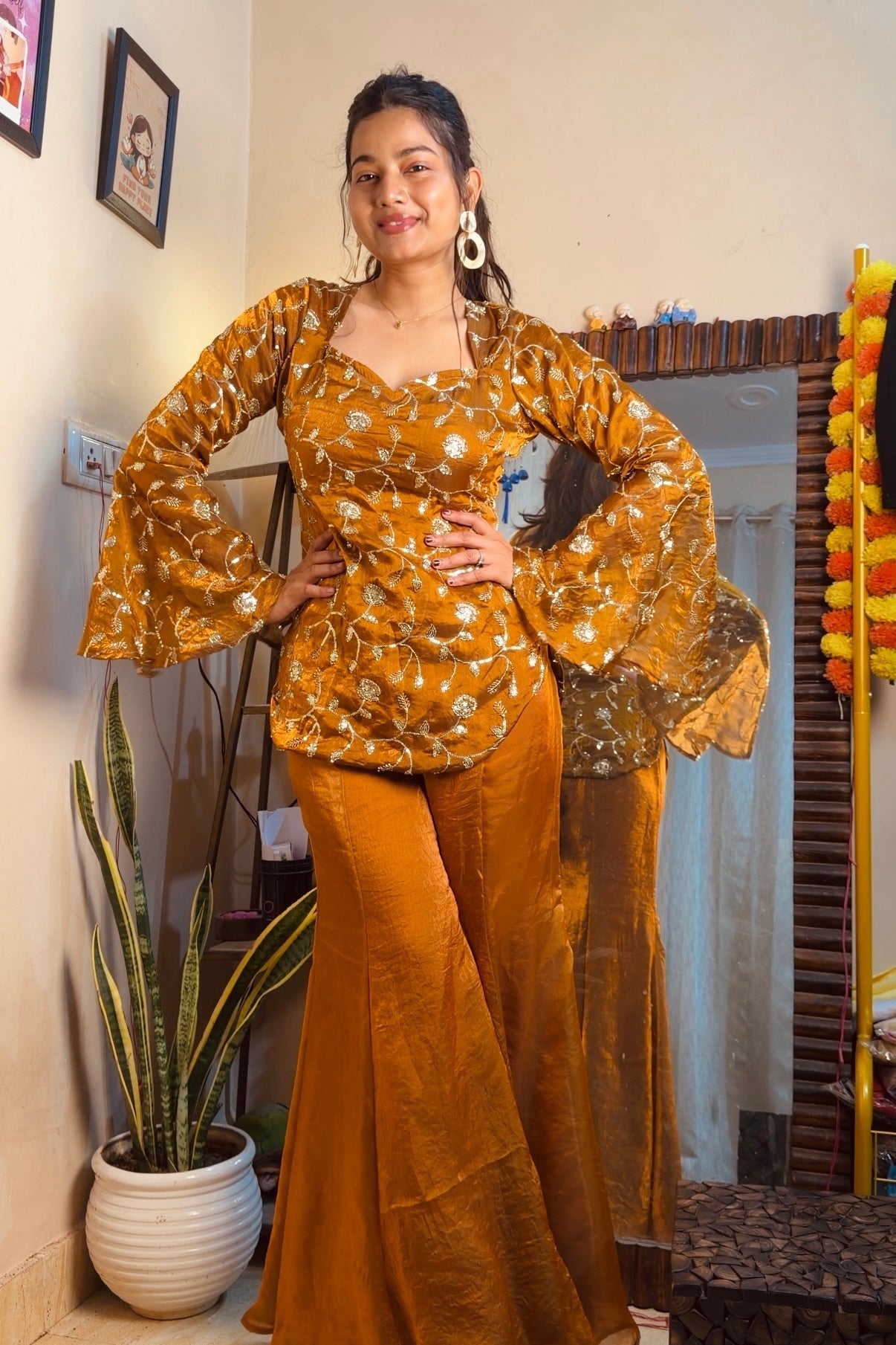 Woman in a mustard yellow traditional outfit standing indoors with decor elements.
