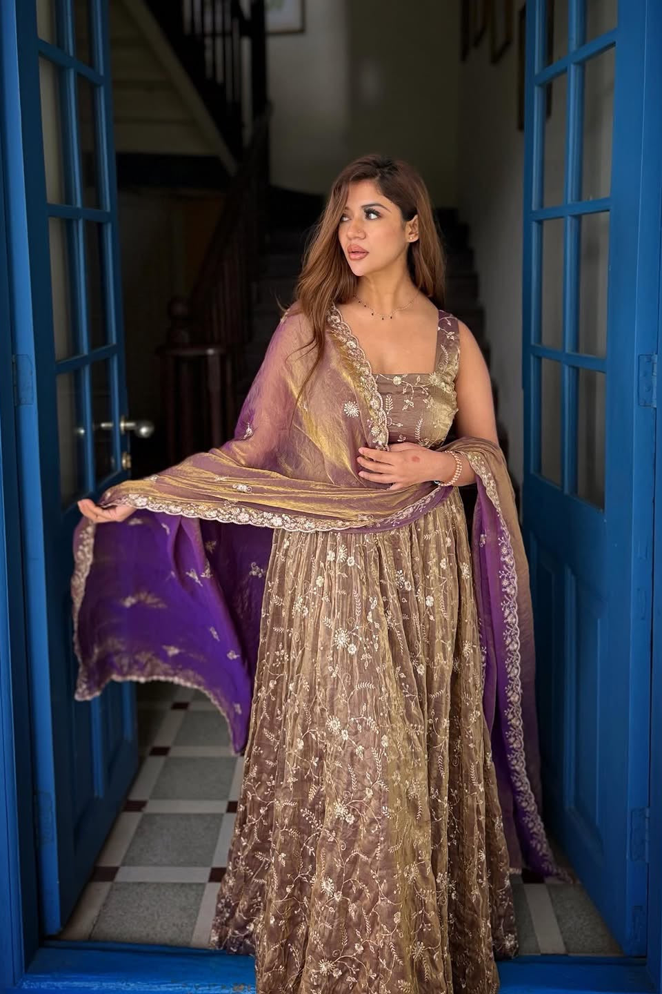 Woman in a traditional outfit standing in a doorway with blue doors.