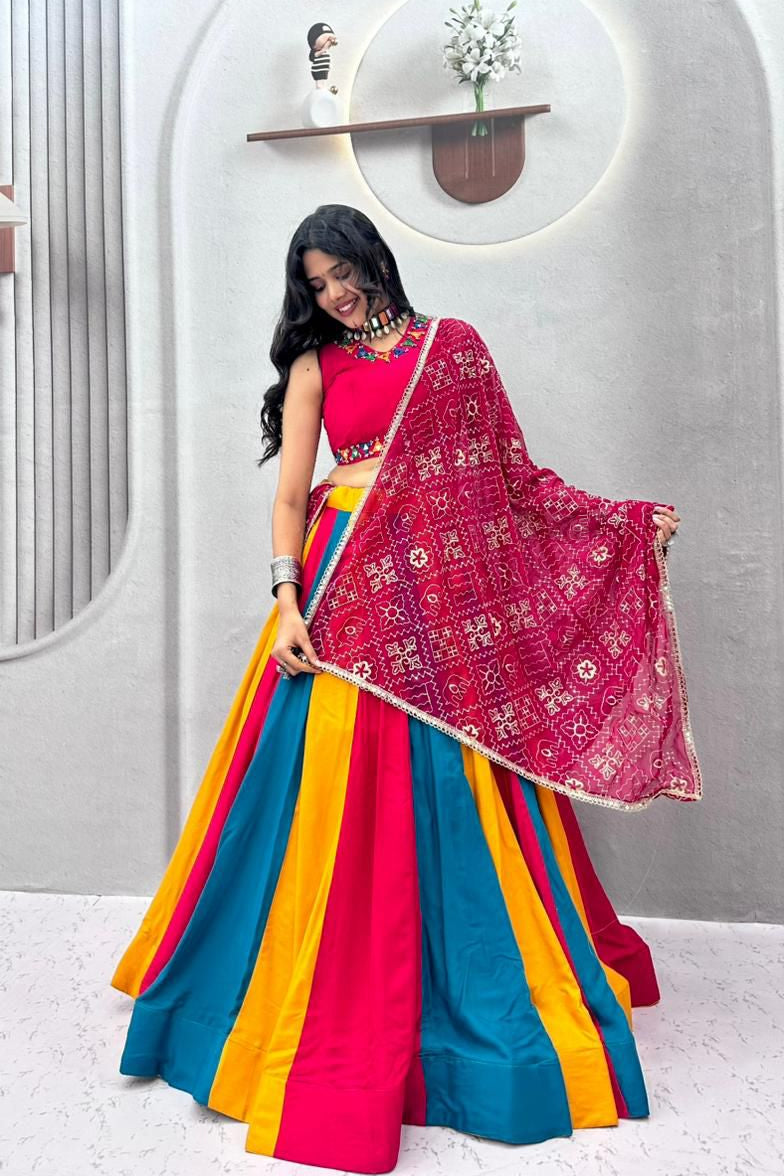 Woman in a colorful traditional outfit with a pink dupatta against a white wall.