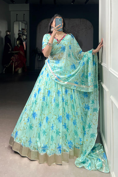 Person wearing a light blue floral saree in a room.