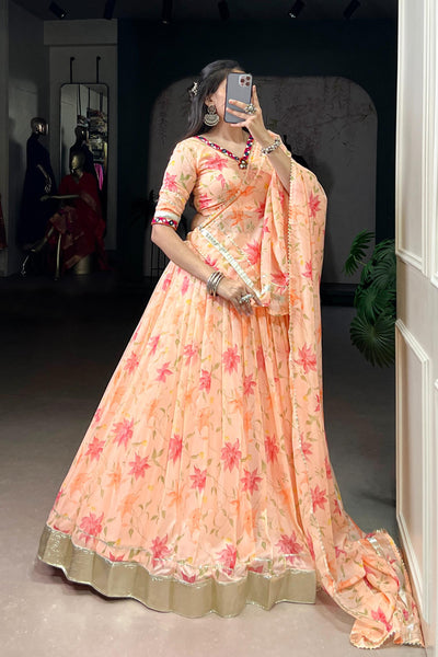 Woman in a peach floral saree taking a mirror selfie indoors.